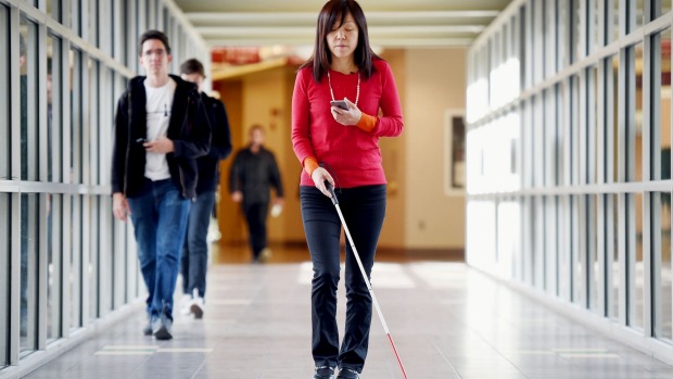 Blind Women in a hallway using cane and smart phone to get around.