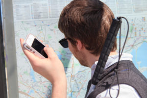 Young blind man at a bus stop using assistive technology to help with map