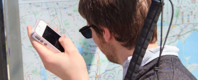 Young blind man at a bus stop using assistive technology to help with map